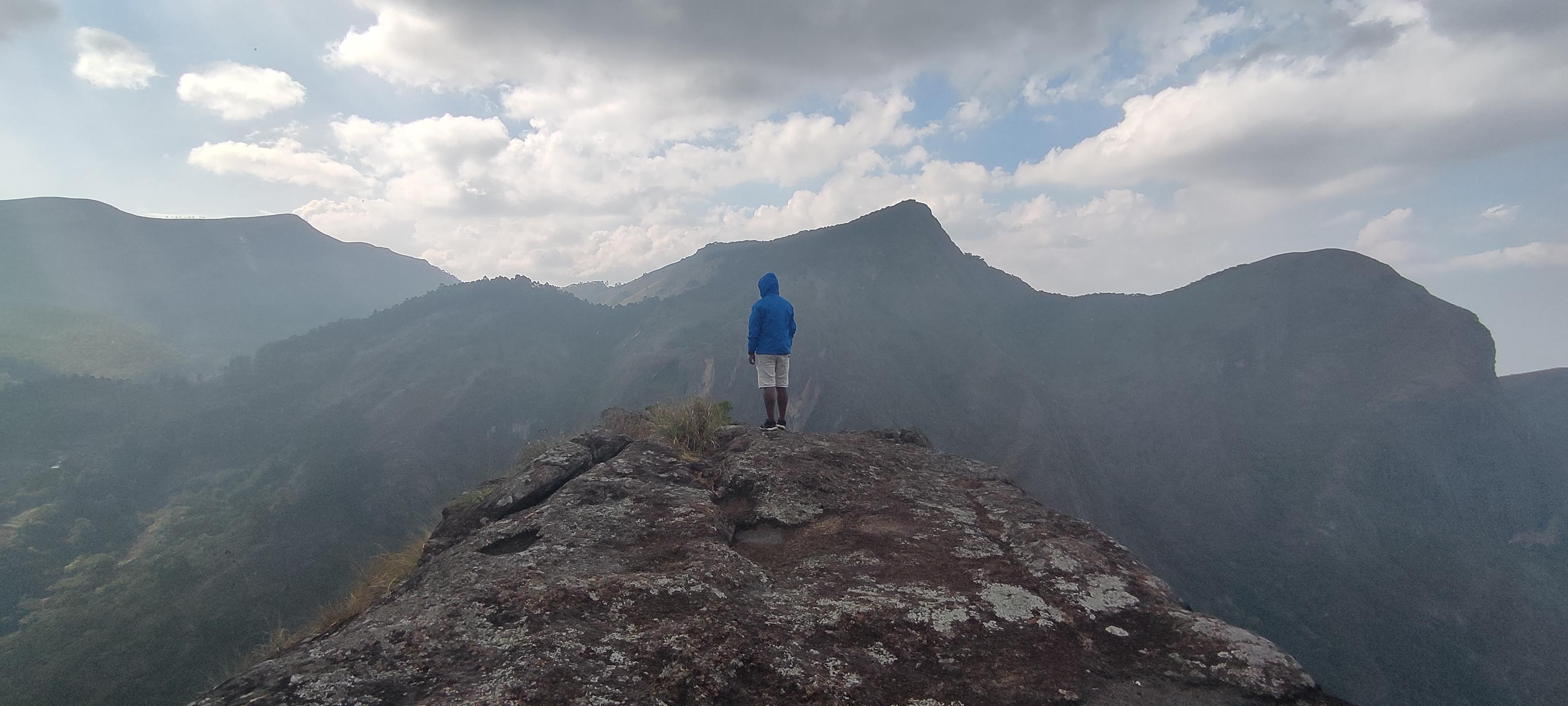 Hiker standing on a rocky summit with panoramic Western Ghats ridgeline
